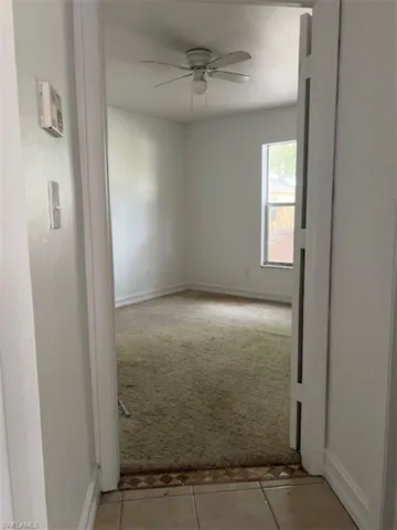 Unfurnished room featuring light tile patterned floors, light colored carpet, and ceiling fan