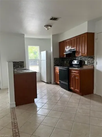 Kitchen with freestanding refrigerator, stove, light tile patterned floors, decorative backsplash, and exhaust hood