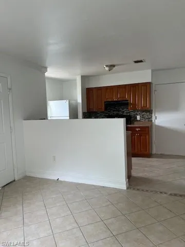 Kitchen with fridge, backsplash, light tile patterned flooring, crown molding, and brown cabinetry