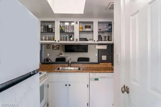 Bar with white cabinetry, sink, white appliances, and dark stone countertops