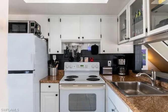Kitchen featuring sink, white cabinets, white appliances, and decorative backsplash