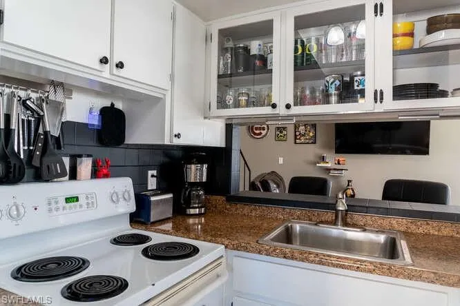 Kitchen featuring white cabinetry, white electric stove, sink, and backsplash