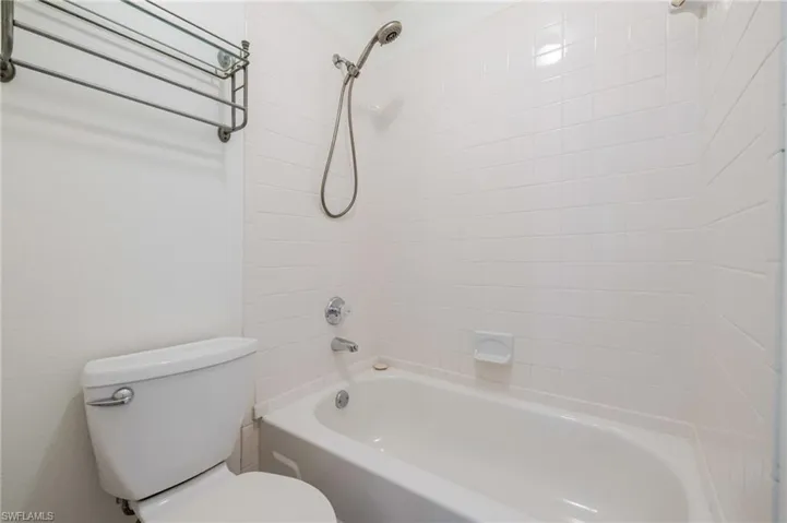 Bathroom featuring a white bathtub with tile surround, a chrome showerhead and faucet, and a white toilet