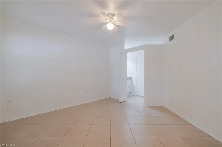 Spacious room featuring neutral-toned tile flooring, white walls, and a ceiling fan with integrated lighting