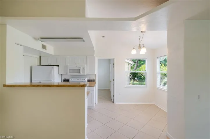 Open-concept kitchen and dining area featuring white cabinetry, white appliances, a breakfast bar, and tile flooring
