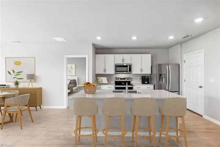 Virtually Staged-Kitchen with appliances with stainless steel finishes, white cabinetry, an island with sink, a kitchen breakfast bar, and light stone countertops