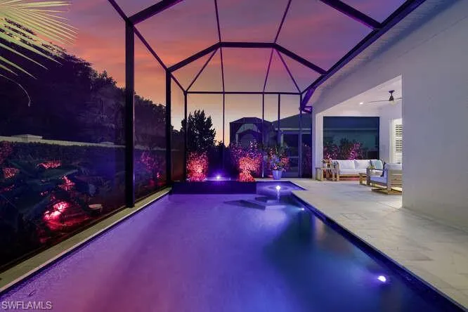 Pool at dusk featuring glass enclosure, ceiling fan, a patio, and an outdoor living space