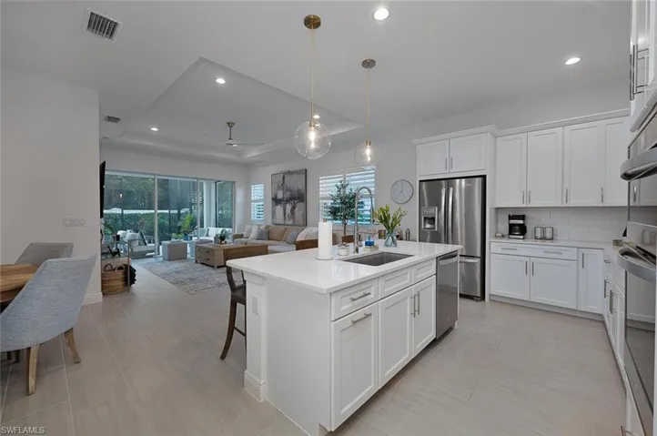 Kitchen with stainless steel appliances, white cabinets, a raised ceiling, a center island with sink, and pendant lighting