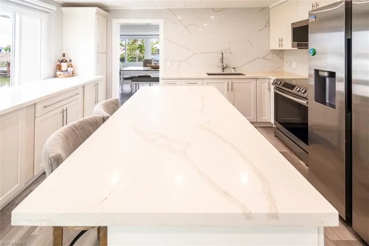 Kitchen featuring light wood-style flooring, white cabinetry, light stone countertops, stainless steel appliances, and a kitchen breakfast bar