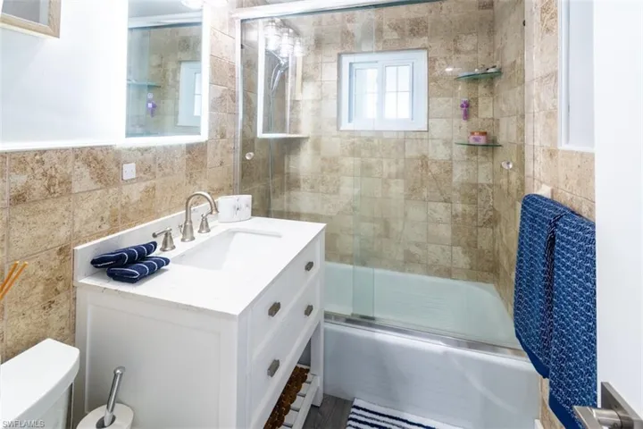 Bathroom featuring vanity, bath / shower combo with glass door, and tile walls