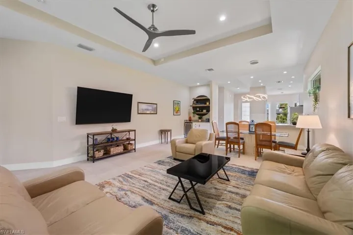Living room featuring ceiling fan, recessed lighting, a tray ceiling, light tile patterned floors, and a chandelier