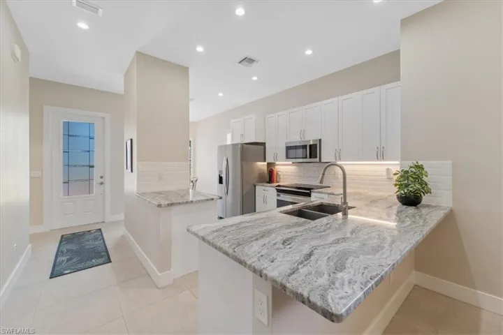 Kitchen with stainless steel appliances, a peninsula, backsplash, light stone counters, and white cabinets