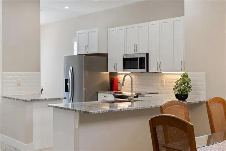 Kitchen featuring stainless steel appliances, a peninsula, light stone countertops, tasteful backsplash, and recessed lighting