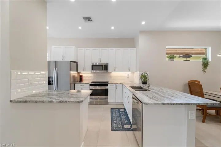 Kitchen featuring appliances with stainless steel finishes, a peninsula, tasteful backsplash, light tile patterned flooring, and white cabinetry