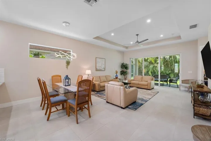 Living area with a raised ceiling, ceiling fan, recessed lighting, and light tile patterned flooring