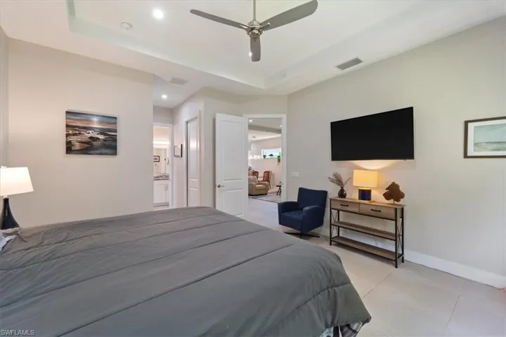 Bedroom with a raised ceiling, light tile patterned flooring, connected bathroom, recessed lighting, and a ceiling fan