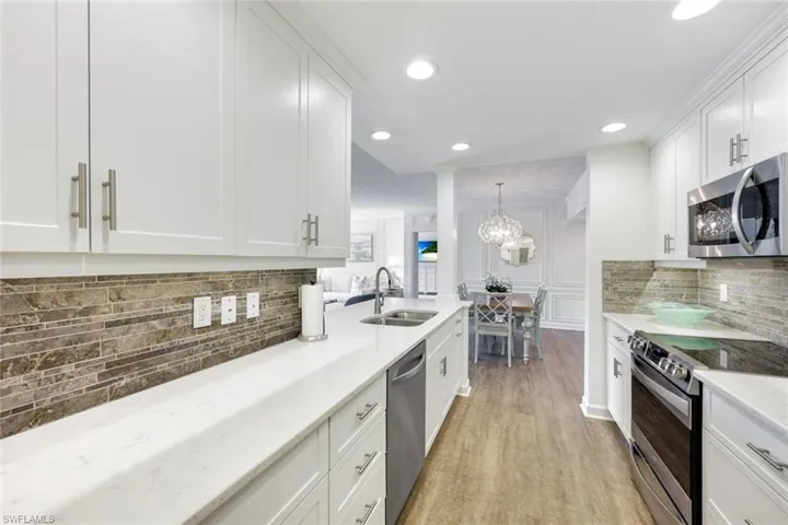 Kitchen featuring stainless steel appliances, backsplash, white cabinets, light stone counters, and light wood-type flooring
