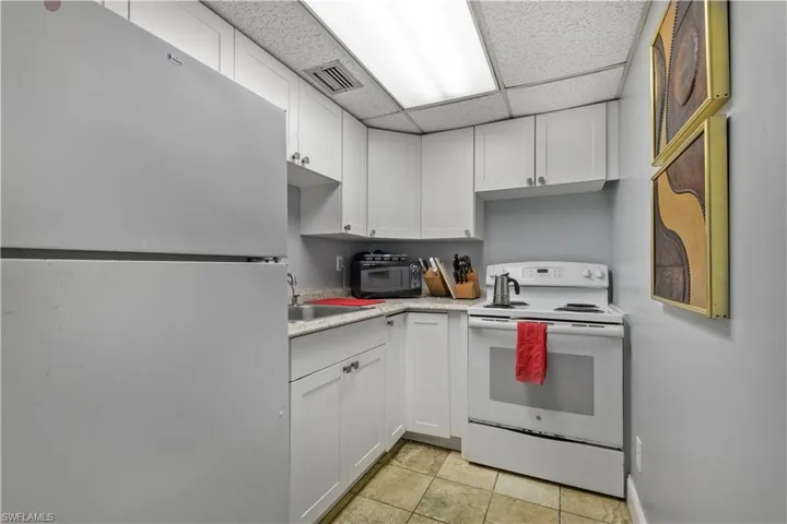 Kitchen with white appliances, a paneled ceiling, white cabinetry, light countertops, and light tile patterned floors
