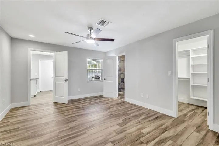 Unfurnished bedroom featuring a spacious closet, light wood-style floors, ensuite bathroom, a ceiling fan, and recessed lighting