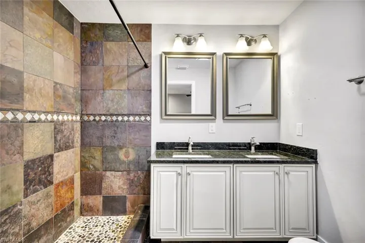 Full bathroom featuring tiled shower and double vanity