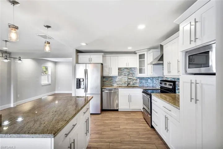Kitchen with stainless steel appliances, decorative light fixtures, glass insert cabinets, a center island, and white cabinetry
