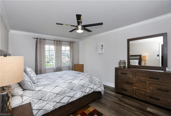 Bedroom featuring a ceiling fan, baseboards, dark wood-type flooring, and crown molding