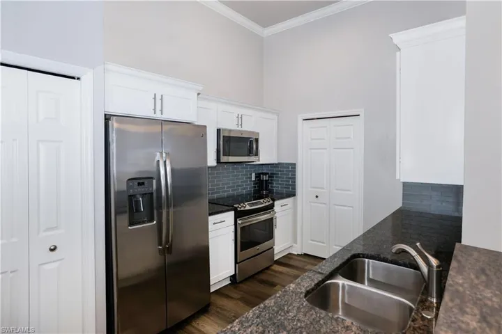 Kitchen with dark wood-type flooring, a sink, ornamental molding, appliances with stainless steel finishes, and tasteful backsplash