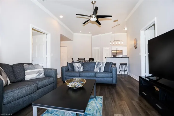 Living area featuring dark wood finished floors, crown molding, baseboards, and ceiling fan