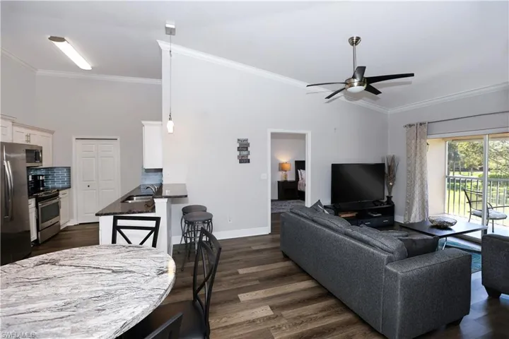 Living room featuring crown molding, baseboards, ceiling fan, and dark wood-style flooring