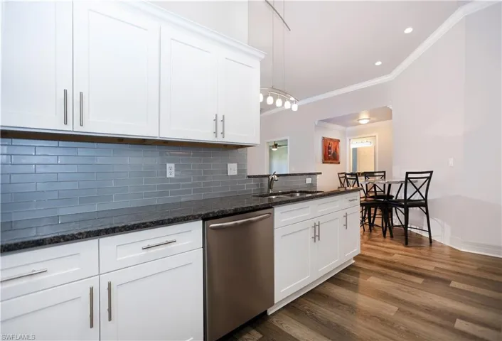Kitchen featuring tasteful backsplash, dishwasher, dark wood-style floors, white cabinetry, and a sink