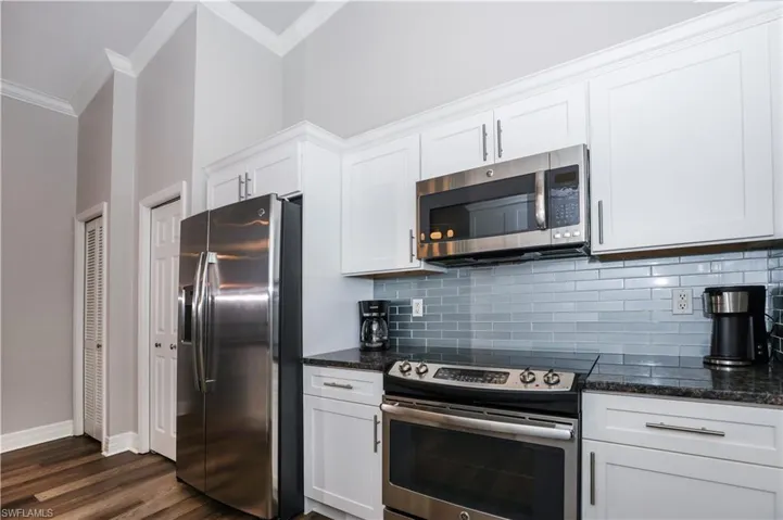 Kitchen with dark wood-style floors, crown molding, stainless steel appliances, backsplash, and white cabinets
