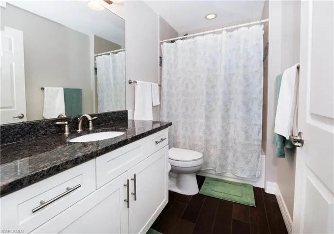 Full bathroom with toilet, wood tiled floor, shower / bath combination with curtain, and vanity