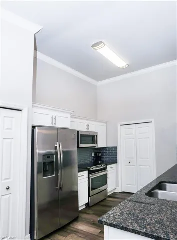 Kitchen with crown molding, appliances with stainless steel finishes, dark wood-type flooring, and backsplash