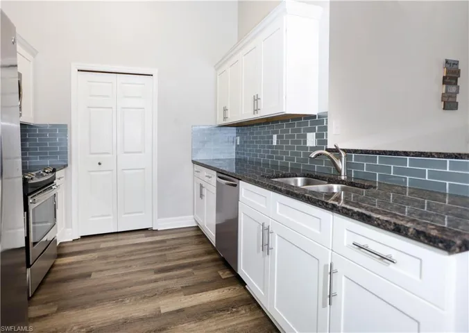 Kitchen featuring white cabinets, dark wood finished floors, appliances with stainless steel finishes, dark stone countertops, and a sink