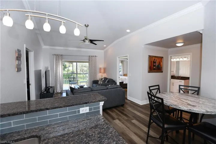 Living area featuring baseboards, a ceiling fan, dark wood-style flooring, vaulted ceiling, and crown molding
