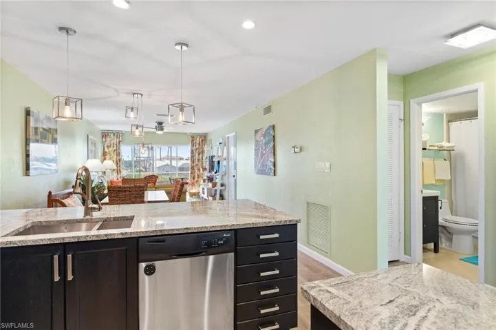 Kitchen featuring stainless steel dishwasher, sink, decorative light fixtures, light wood-type flooring, and light granite countertops.