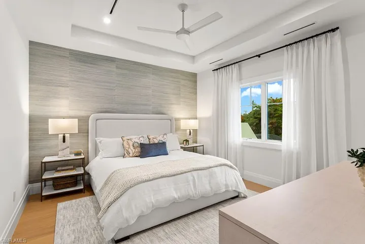 Bedroom with an accent wall, baseboards, a tray ceiling, and light wood-style floors