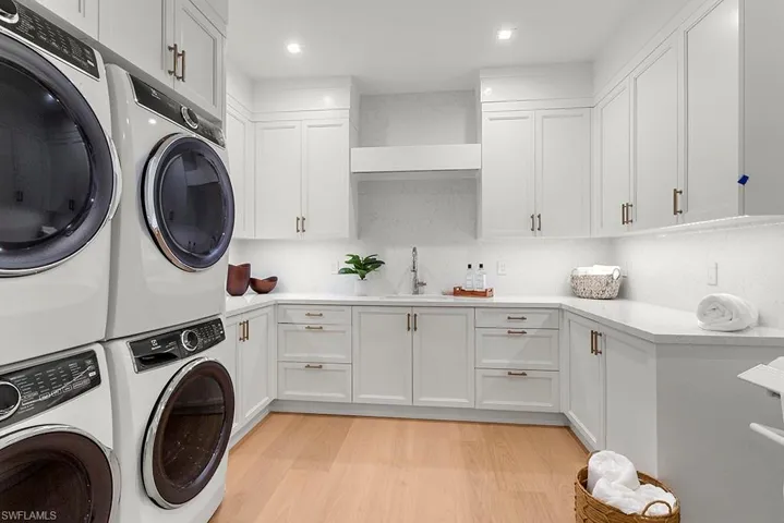 Washroom featuring cabinet space, washer and clothes dryer, stacked washing machine and dryer, light wood-style flooring, and recessed lighting