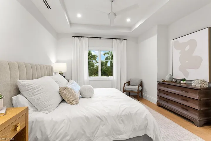 Bedroom featuring light wood finished floors, a tray ceiling, ceiling fan, baseboards, and recessed lighting