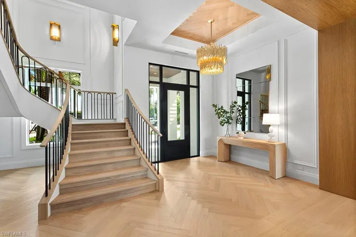 Foyer with stairs, a decorative wall, a chandelier, a tray ceiling, and baseboards