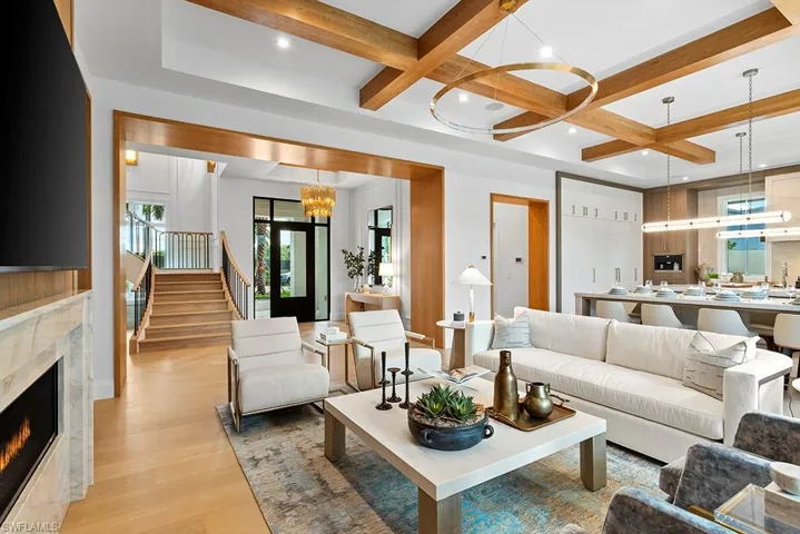 Living area with a chandelier, coffered ceiling, light wood-type flooring, beam ceiling, and stairway