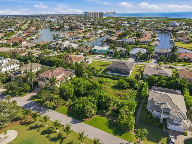 Aerial perspective featuring a waterfront residential community with integrated canal systems, expansive green space, mature palm vegetation, and proximity to coastal waters