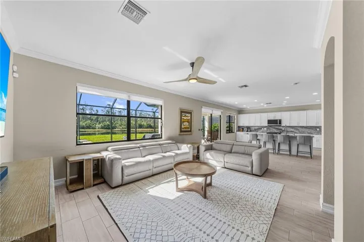 Living room with wood finish floors, crown molding, ceiling fan, recessed lighting, and arched walkways