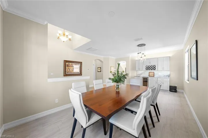 Dining space featuring arched walkways, ornamental molding, a chandelier, light wood-type flooring, and wine cooler