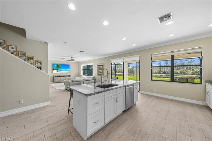 Kitchen with white cabinetry, a kitchen island with sink, light stone counters, a kitchen bar, and crown molding