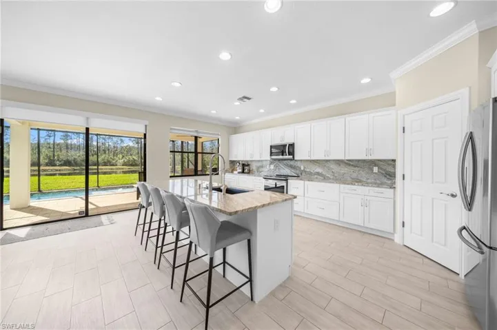 Kitchen with ornamental molding, light stone countertops, appliances with stainless steel finishes, a breakfast bar area, and a kitchen island with sink