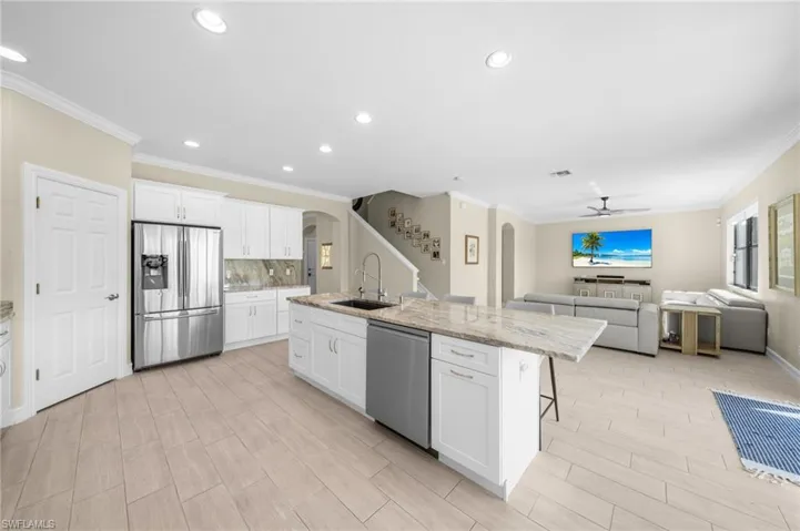 Kitchen featuring arched walkways, appliances with stainless steel finishes, white cabinets, light stone counters, and crown molding