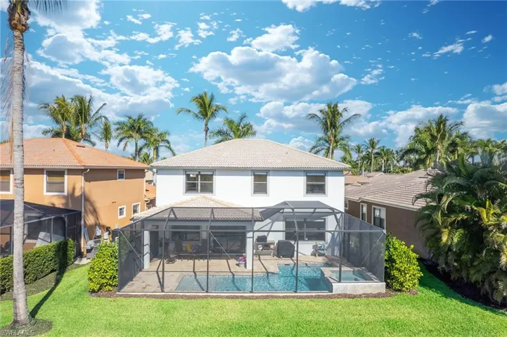 Rear view of property with glass enclosure, a tile roof, a sunroom, and a lawn