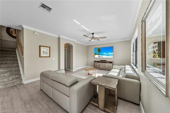 Living area featuring arched walkways, ornamental molding, stairs, ceiling fan, and wood finish floors