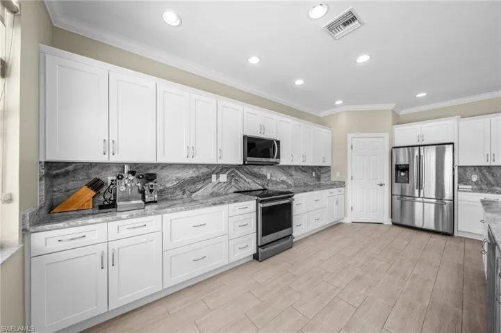 Kitchen featuring appliances with stainless steel finishes, white cabinets, decorative backsplash, crown molding, and light stone counters
